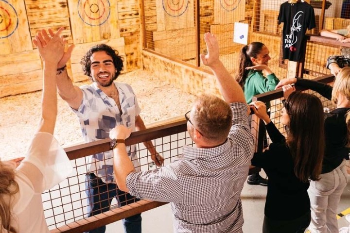 People celebrating at an indoor axe throwing venue, high-fiving over a barrier.