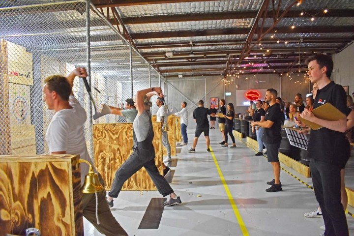 People throwing axes at targets in an indoor venue with spectators.