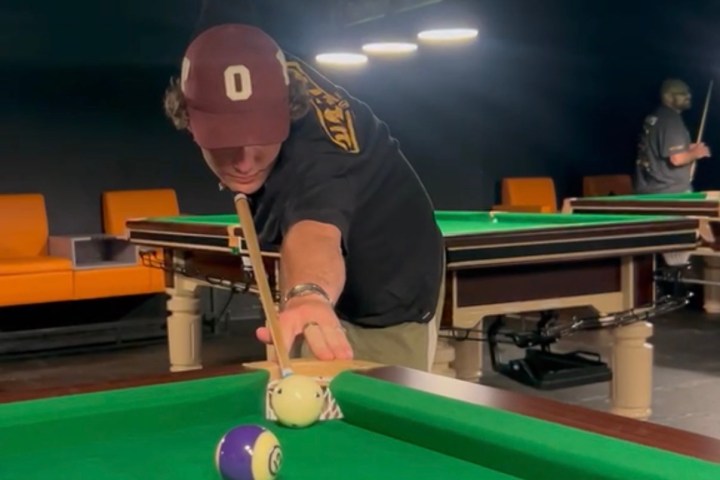 Person aiming a shot in a dimly lit pool hall.