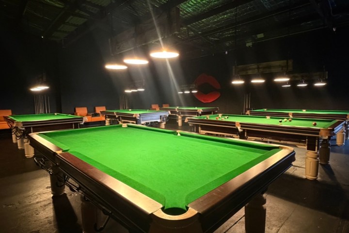 Dimly lit room with several green-covered pool tables.